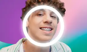 Ragazzo con cera apparecchio, sorride con un cerchio luminoso attorno al viso. Sfondo sfumato viola e verde.