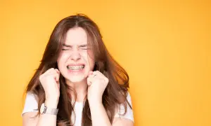 Ragazza con apparecchio ai denti, espressione di sforzo, mani strette. Un'immagine che evoca il percorso delle labbra prima e dopo apparecchio.
