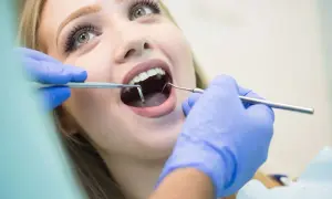 Visita dentistica: una giovane donna con un sorriso smagliante apre la bocca mentre il dentista esamina i suoi denti con strumenti, incluso uno specchietto che riflette il foro mentoniero.
