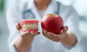 Un dentista mostra un modello di denti e una mela, suggerendo cibi che fanno male ai denti.