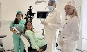 Sorrisi in clinica: un dentista, due assistenti e una paziente felice. La prima visita dal dentista si paga, ma la salute orale è un investimento.