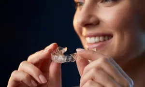 Donna sorridente tiene in mano allineatori dentali trasparenti, pronti per un sorriso perfetto.