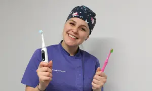 Sorriso smagliante di un dentista con cappellino a tema natalizio, che mostra uno spazzolino elettrico e uno manuale. Si può usare lo spazzolino elettrico con l'apparecchio.