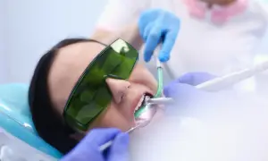 Paziente con occhiali protettivi verdi durante un intervento dentistico. Le mani guantate del dentista lavorano sulla bocca. Esperienze di apicectomia.