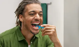 Uomo con dreadlocks usa una forcella tendifilo interdentale blu per pulire i denti.