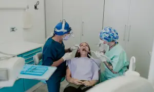 Un dentista con lampada frontale e un assistente eseguono una procedura, forse un'anestesia dentista, su una paziente seduta sulla poltrona.