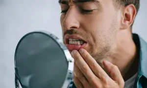 Uomo preoccupato osserva i suoi denti che si spostano a 50 anni, toccandosi la gengiva con un dito.