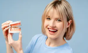 Ragazza sorridente con apparecchio dentale tiene un modello di denti. Chiediti ogni quanto si stringe l'apparecchio per un sorriso perfetto.