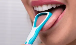 Una persona usa un puliscilingua azzurro per pulire la lingua, un gesto che ricorda la lava lingua.