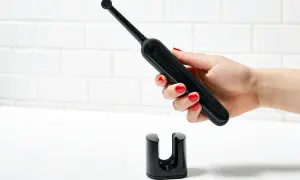 Mano con smalto rosso tiene uno spazzolino elettrico nero sopra il suo supporto. Un modo efficace per pulire muffa spazzolino elettrico.