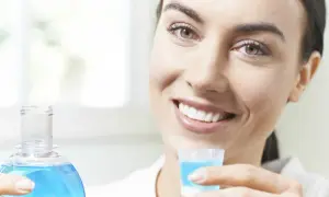 Woman smiling, holding a bottle of blue mouthwash and a cap filled with mouthwash.