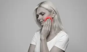Donna con dolore alla mascella, evidenziato in rosso. Le conseguenze di una mandibola fuori asse possono essere debilitanti.