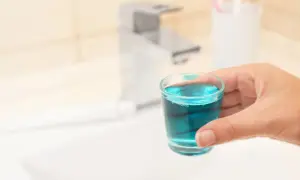Mano tiene bicchierino con collutorio azzurro, ideale per l'igiene orale in gravidanza.