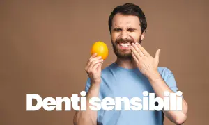 Uomo con espressione sofferente, tiene un'arancia e si tocca la guancia, mostrando la sua sensibilità dentale.