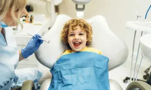 Bambino sorridente dal dentista, pronto per un controllo. Il dentista, con guanti blu, tiene uno specchietto, forse per mostrare cos'è il fluoro e la sua importanza per i denti.