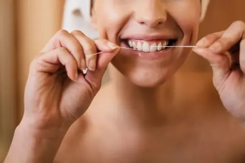 Donna sorridente che mostra come usare il filo interdentale per una pulizia profonda dei denti.