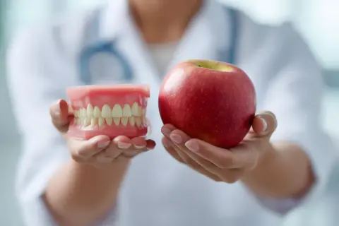 Un dentista mostra un modello di denti e una mela, suggerendo cibi che fanno male ai denti.