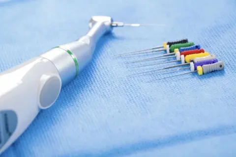 Strumenti endodontici colorati e un manipolo dentale, pronti per un trattamento di canal root sealer.