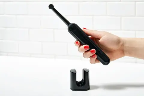 Mano con smalto rosso tiene uno spazzolino elettrico nero sopra il suo supporto. Un modo efficace per pulire muffa spazzolino elettrico.