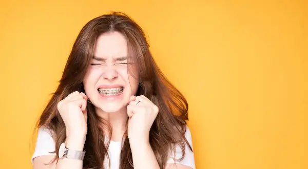 Ragazza con apparecchio ai denti, espressione di sforzo, mani strette. Un'immagine che evoca il percorso delle labbra prima e dopo apparecchio.