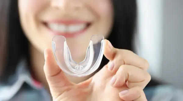 Donna sorride mostrando un bite trasparente. Scopri quanto costa un bite dal dentista per proteggere i tuoi denti.