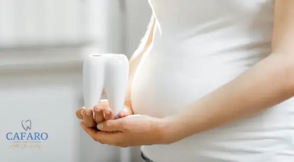 Mani di donna incinta tengono un dente bianco, simbolo della cura per la pulizia dei denti in gravidanza.