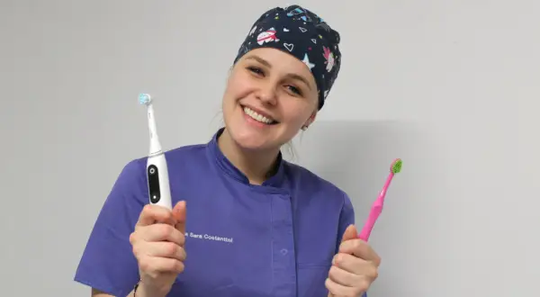 Sorriso smagliante di un dentista con cappellino a tema natalizio, che mostra uno spazzolino elettrico e uno manuale. Si può usare lo spazzolino elettrico con l'apparecchio.