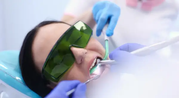 Paziente con occhiali protettivi verdi durante un intervento dentistico. Le mani guantate del dentista lavorano sulla bocca. Esperienze di apicectomia.