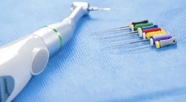 Strumenti endodontici colorati e un manipolo dentale, pronti per un trattamento di canal root sealer.