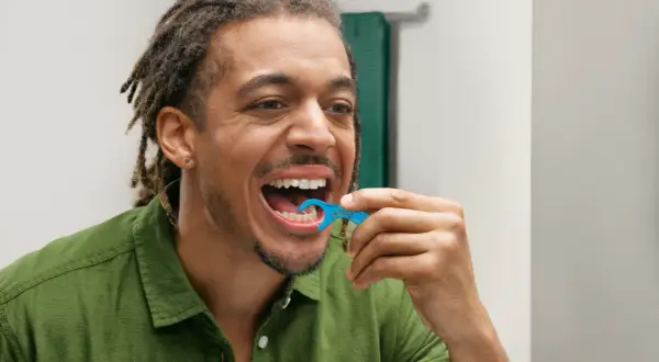Uomo con dreadlocks usa una forcella tendifilo interdentale blu per pulire i denti.