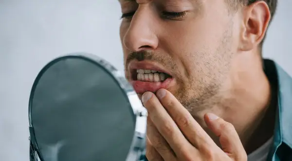 Uomo preoccupato osserva i suoi denti che si spostano a 50 anni, toccandosi la gengiva con un dito.
