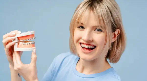 Ragazza sorridente con apparecchio dentale tiene un modello di denti. Chiediti ogni quanto si stringe l'apparecchio per un sorriso perfetto.