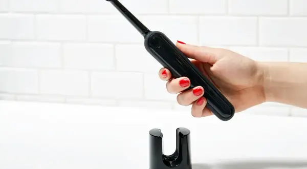 Mano con smalto rosso tiene uno spazzolino elettrico nero sopra il suo supporto. Un modo efficace per pulire muffa spazzolino elettrico.