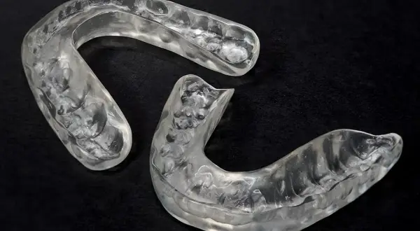 Due bite occlusali trasparenti, sagomati per adattarsi all'arcata dentale, su sfondo nero.