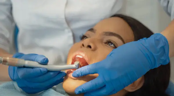 Dottoressa esegue scaling dentale su paziente. Mani con guanti blu tengono strumento odontoiatrico.