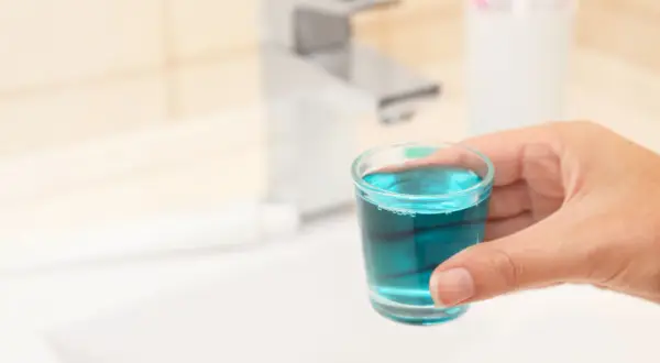 Mano tiene bicchierino con collutorio azzurro, ideale per l'igiene orale in gravidanza.