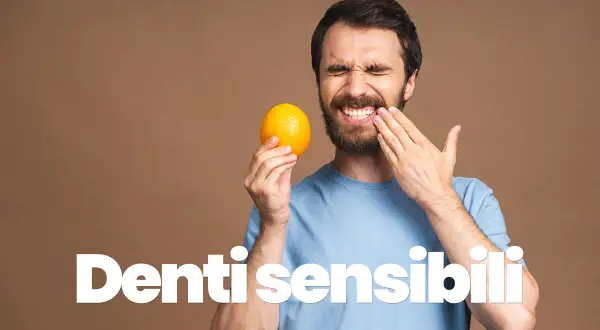 Uomo con espressione sofferente, tiene un'arancia e si tocca la guancia, mostrando la sua sensibilità dentale.