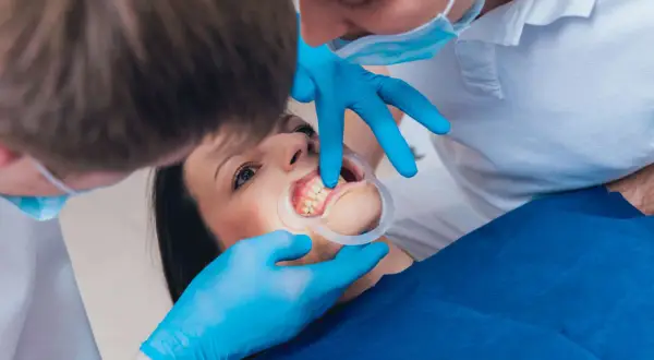 Dentista esamina i denti di una paziente, che ha un divaricatore in bocca. I mammelloni denti sono ben visibili.