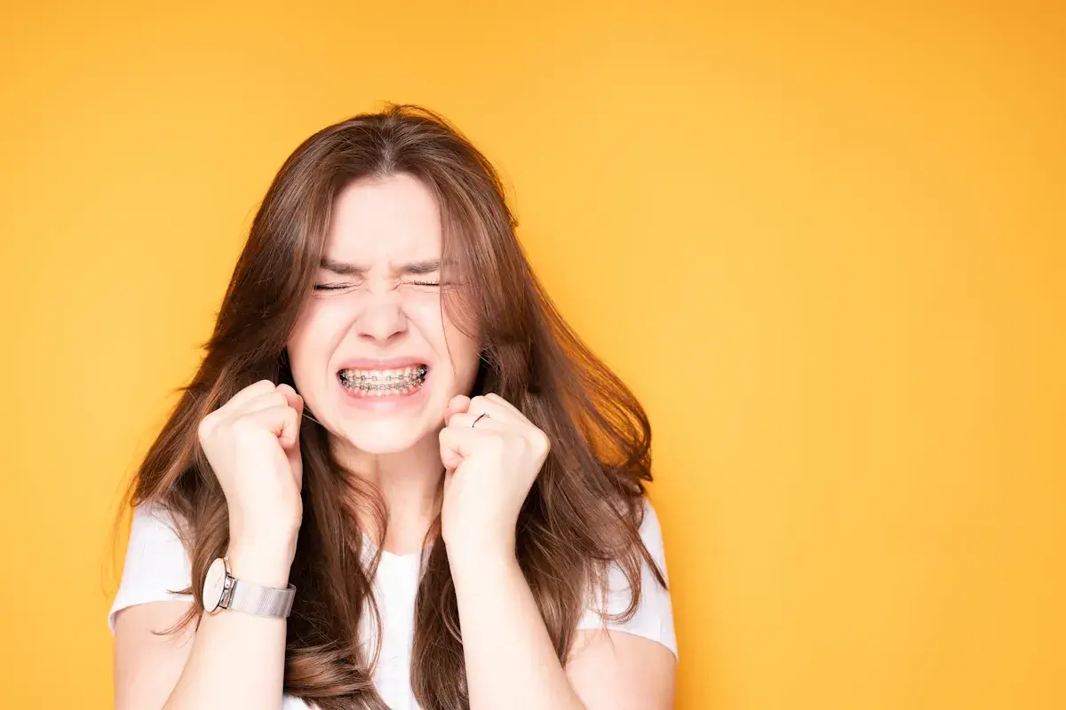 Ragazza con apparecchio ai denti, espressione di sforzo, mani strette. Un'immagine che evoca il percorso delle labbra prima e dopo apparecchio.