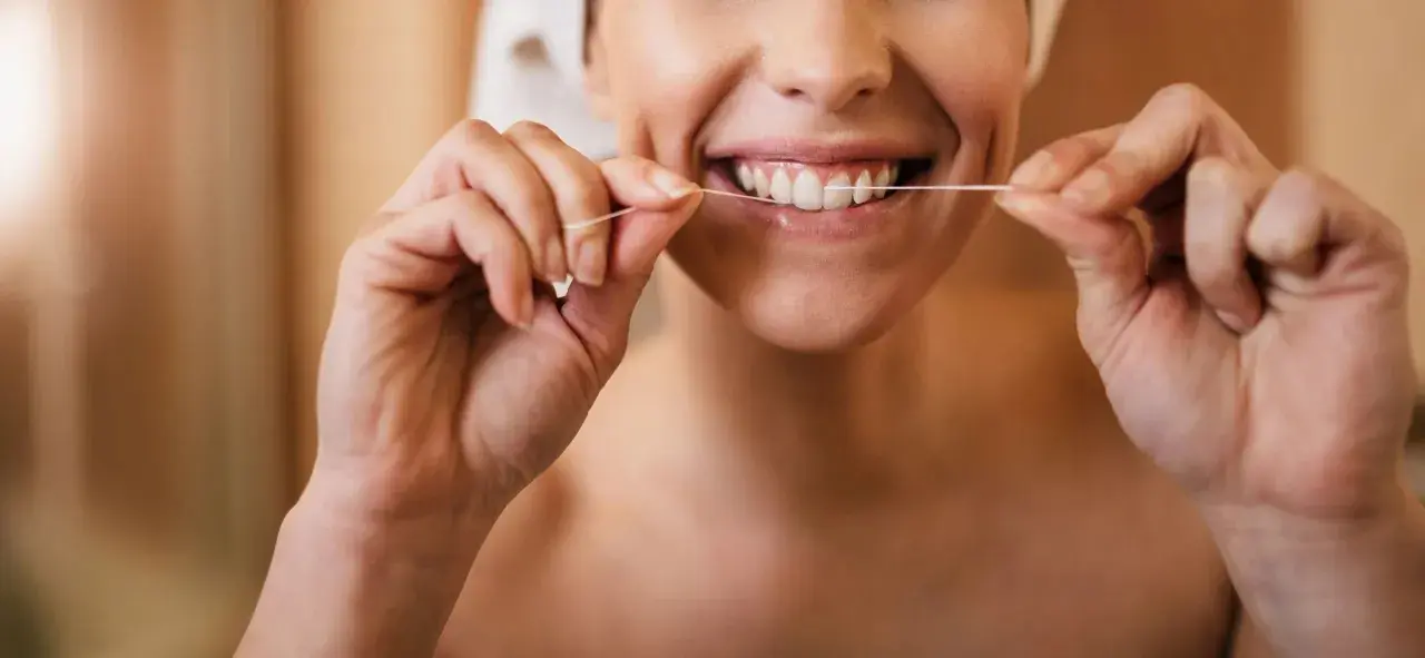Donna sorridente che mostra come usare il filo interdentale per una pulizia profonda dei denti.