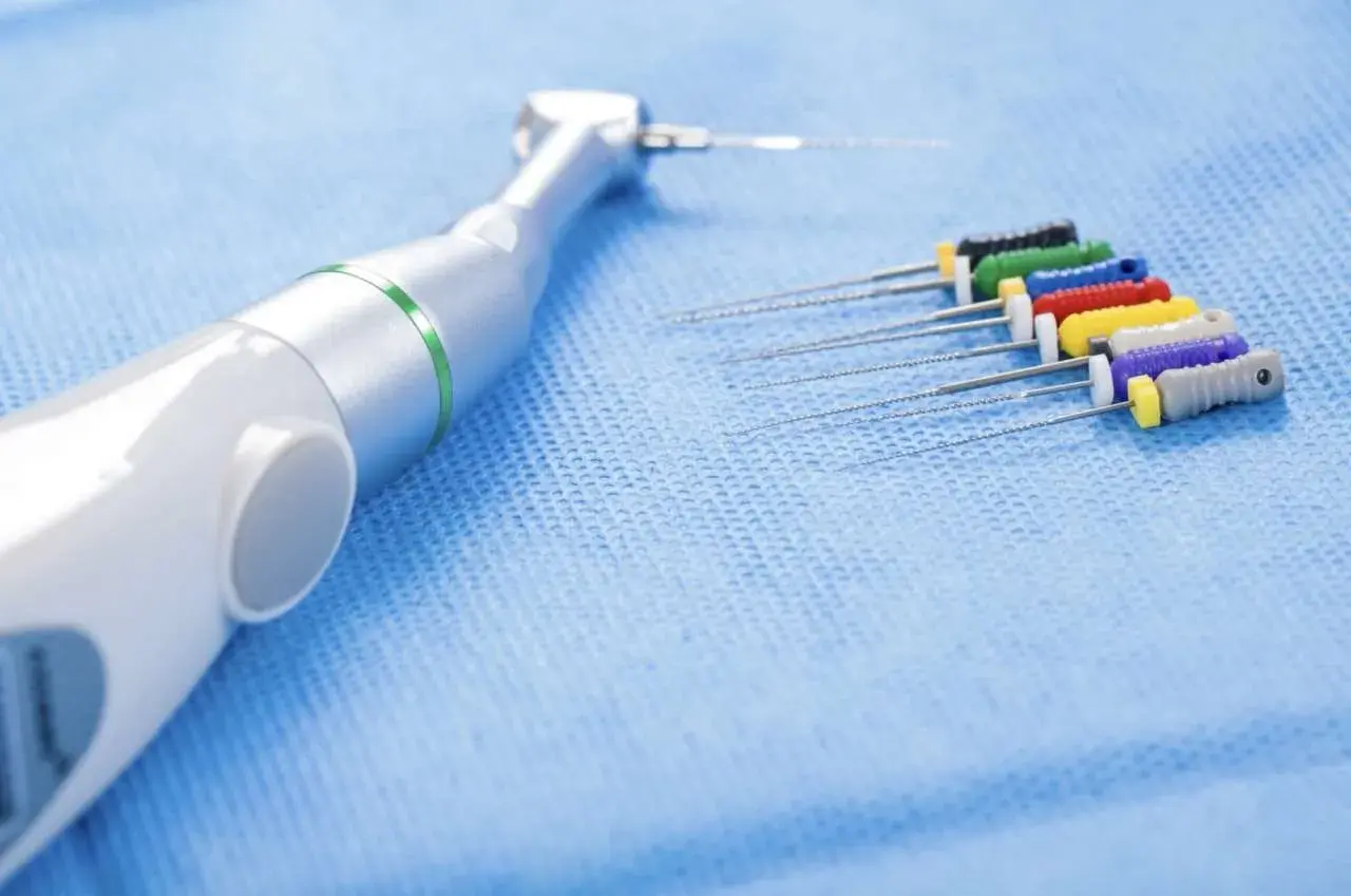 Strumenti endodontici colorati e un manipolo dentale, pronti per un trattamento di canal root sealer.