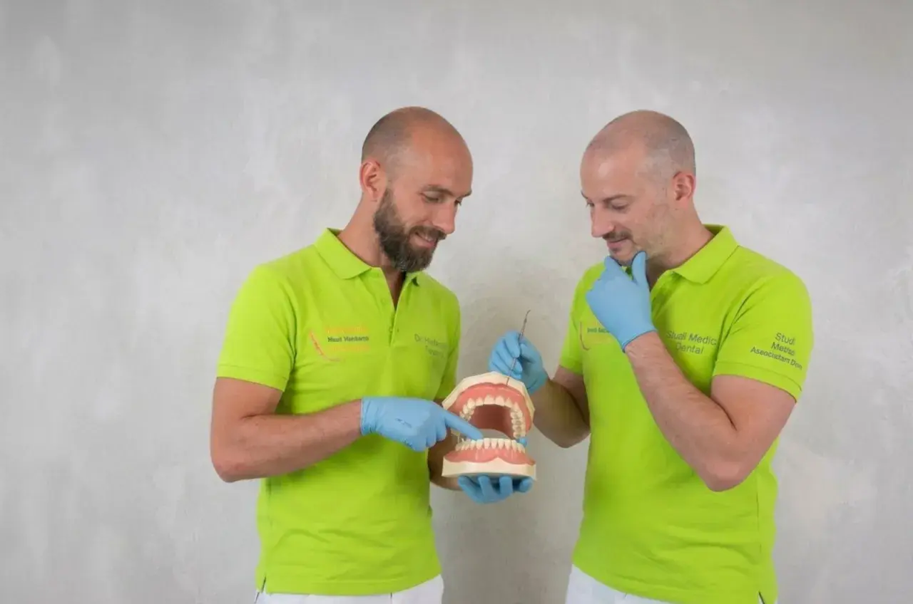 Due dentisti con camici verdi mostrano un modello di denti, spiegando come si chiamano i denti davanti.