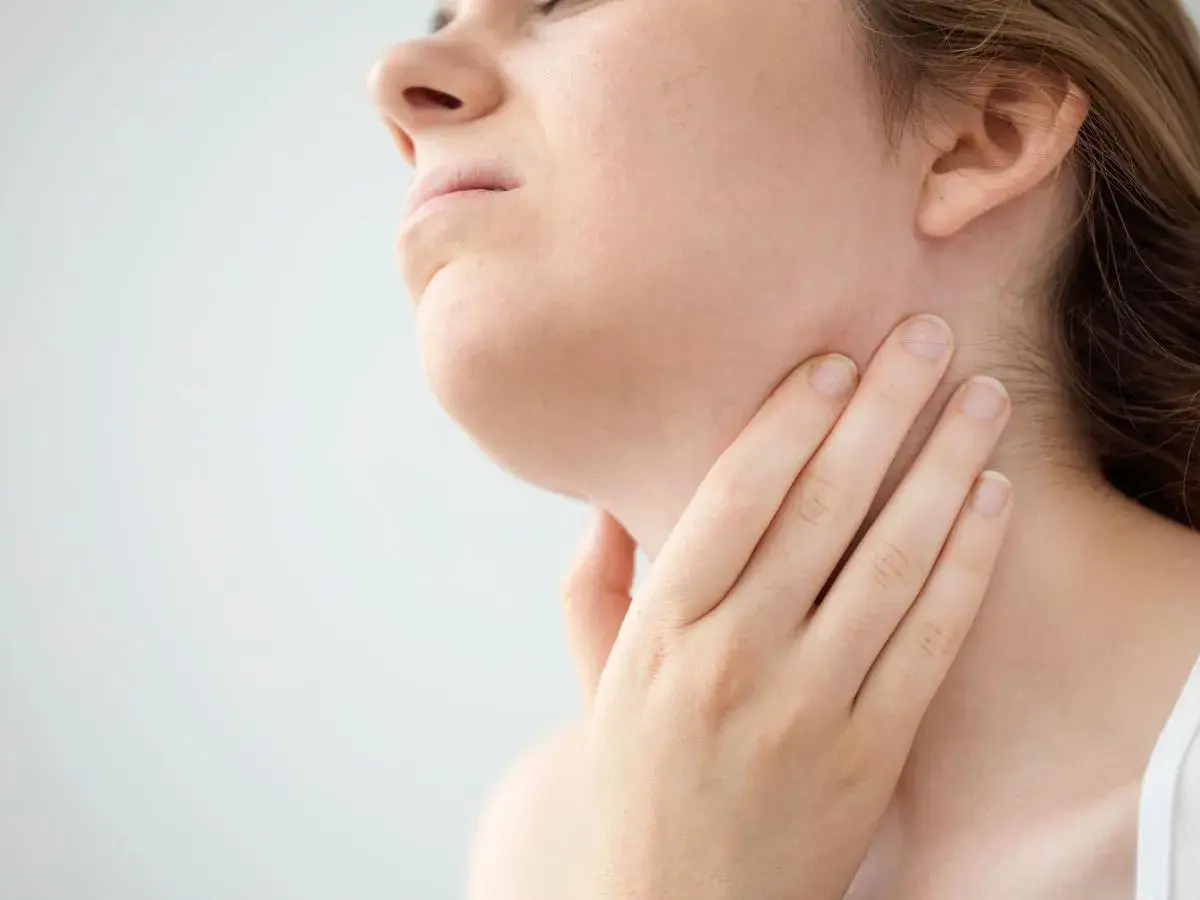 Mano che tocca il collo, forse per sentire i linfonodi sottomentali ingrossati.