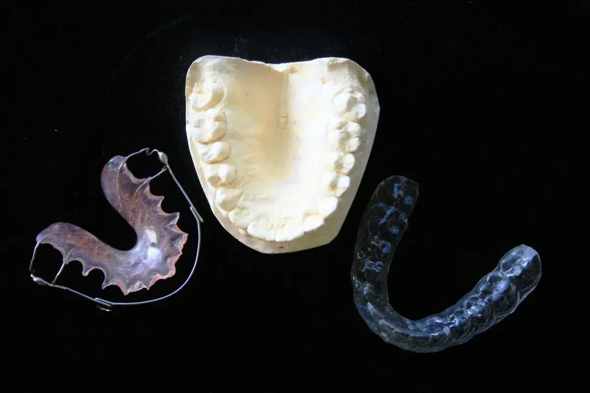 Modello dentale e apparecchi ortodontici, inclusi apparecchi invisibili per adulti, su sfondo nero.