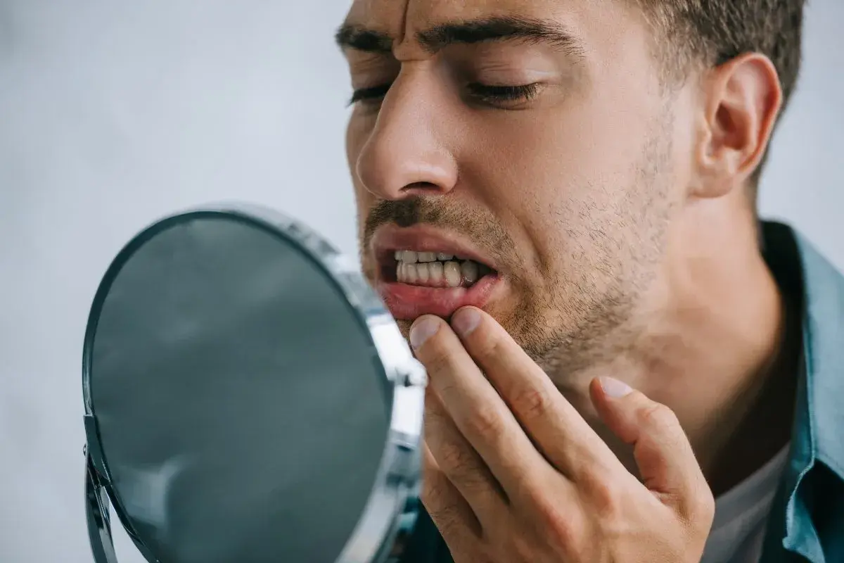 Uomo preoccupato osserva i suoi denti che si spostano a 50 anni, toccandosi la gengiva con un dito.
