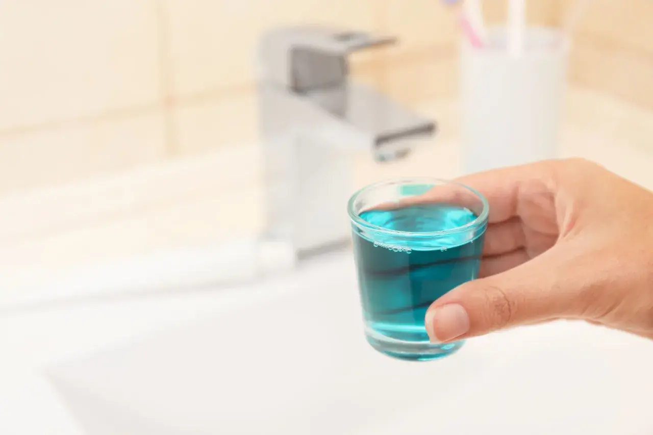 Mano tiene bicchierino con collutorio azzurro, ideale per l'igiene orale in gravidanza.