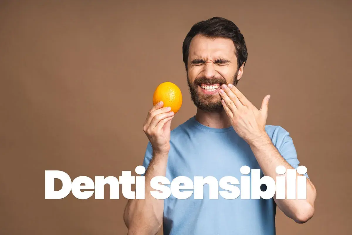 Uomo con espressione sofferente, tiene un'arancia e si tocca la guancia, mostrando la sua sensibilità dentale.