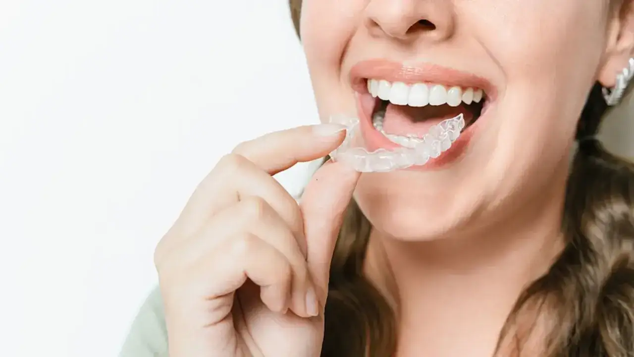 Donna sorridente mostra come togliere Invisalign, un apparecchio trasparente per denti perfetti.