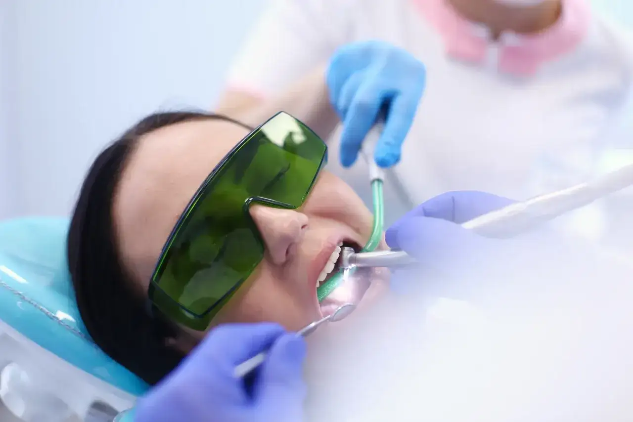Paziente con occhiali protettivi verdi durante un intervento dentistico. Le mani guantate del dentista lavorano sulla bocca. Esperienze di apicectomia.