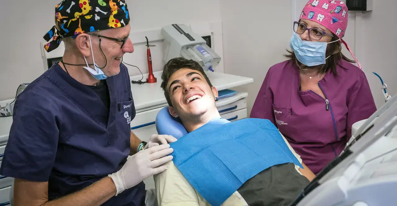 Un dentista e un'assistente sorridono a un giovane paziente, pronto a curare la carie con professionalità e un tocco di allegria.